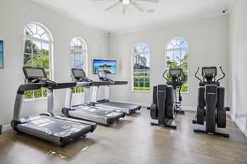 four treadmills in a room with windows and cardio equipment at The Falls of Portofino Apartment, Naples, Florida